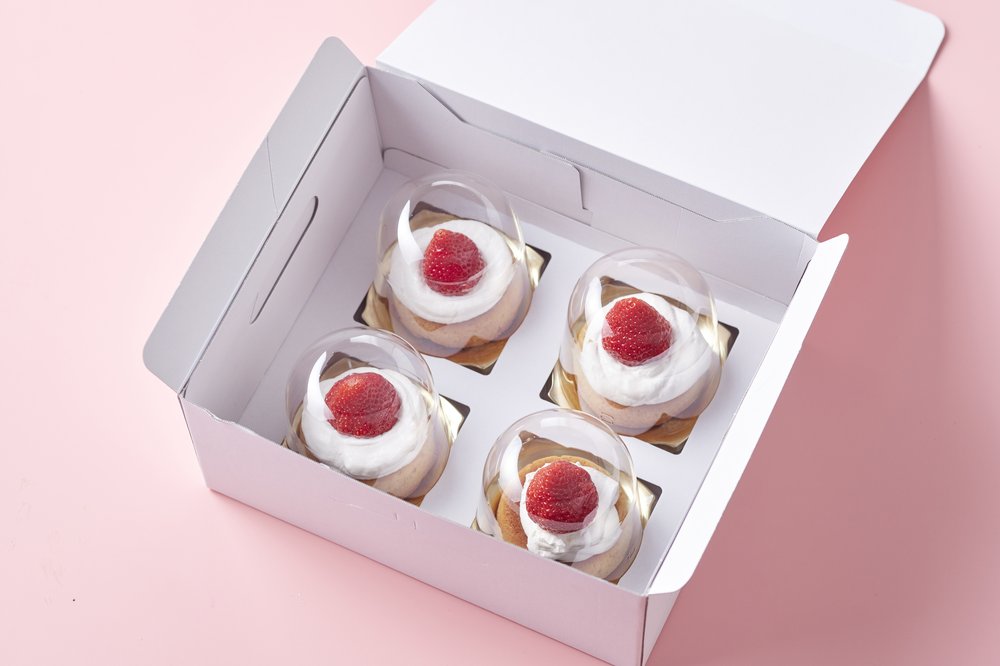 Box of four donuts topped with cream and a strawberry