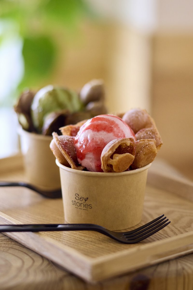 Two bubble waffle cups topped with gelato on a wooden tray